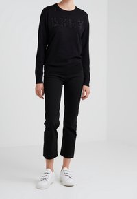 Svart tröja med texturerad "DKNY"-bokstavering, parat med svarta korta byxor och vita sneakers. Enkel design med avslappnad passform.