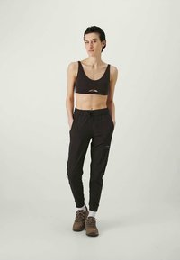 Melnas sporta topiņš ar izgriezumu, savienots ar melniem šauriem jogeriem un brūniem pārgājienu apaviem. Gluda tekstūra, elastīga josta, minimālistisks dizains.