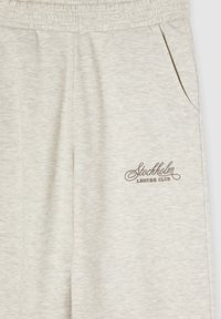 Jasnoszare spodnie dresowe z elastycznym pasem, kieszeniami po bokach oraz wyszywanym logo "Stockholm Leisure Club" w kolorze brązowym. Miękka tekstura.