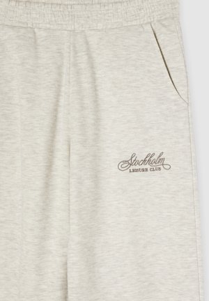 Pantaloni sweat grigi chiari con cintura elastica, tasca laterale e logo ricamato "Stockholm Leisure Club" in marrone. Tessuto morbido.
