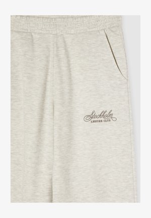 Pantaloni sweat grigi chiari con cintura elastica, tasca laterale e logo ricamato "Stockholm Leisure Club" in marrone. Tessuto morbido.