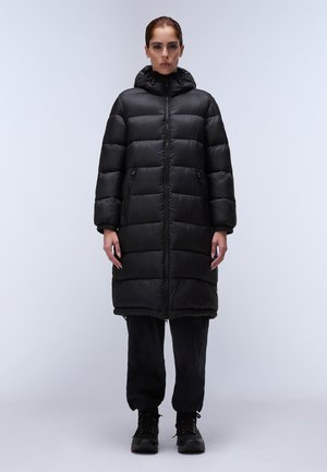 Schwarze Pufferjacke mit Kapuze, mit einem horizontalen Steppmuster, Frontreißverschluss und seitlichen Taschen; getragen über schwarzen Hosen und Stiefeln.