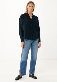 Czarna koszula na guziki z kieszenią, długimi rękawami i luźnym krojem, połączona z jasnoniebieskimi dżinsami o prostym kroju z bocznymi rozporkami.