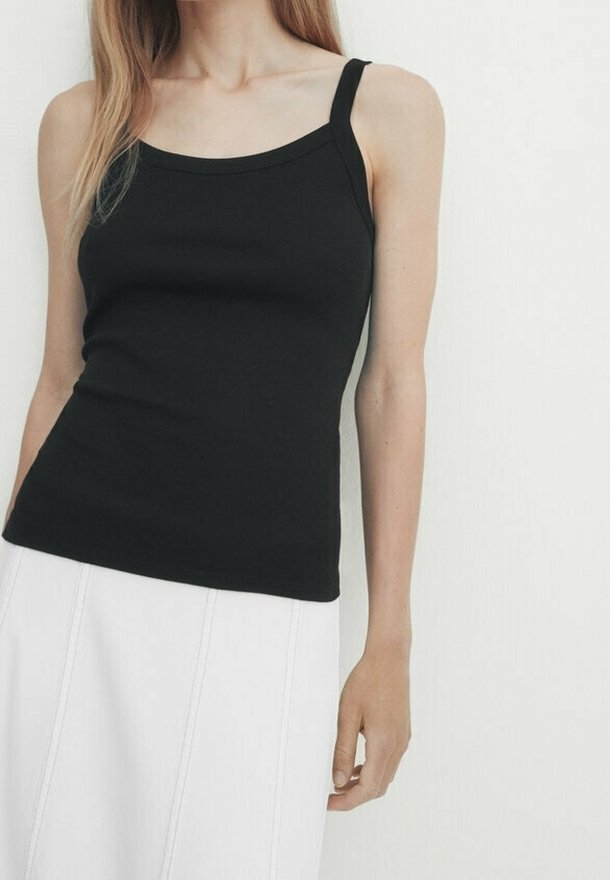 Top noir sans manches en matière douce avec un décolleté en U et des fines bretelles, associé à une jupe blanche unie.
