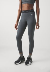 Szare legginsy sportowe z teksturowanym wzorem, z czarnym paskiem w talii oznaczonym "PRO NIKE" oraz czarnymi sneakersami i szarymi skarpetkami.