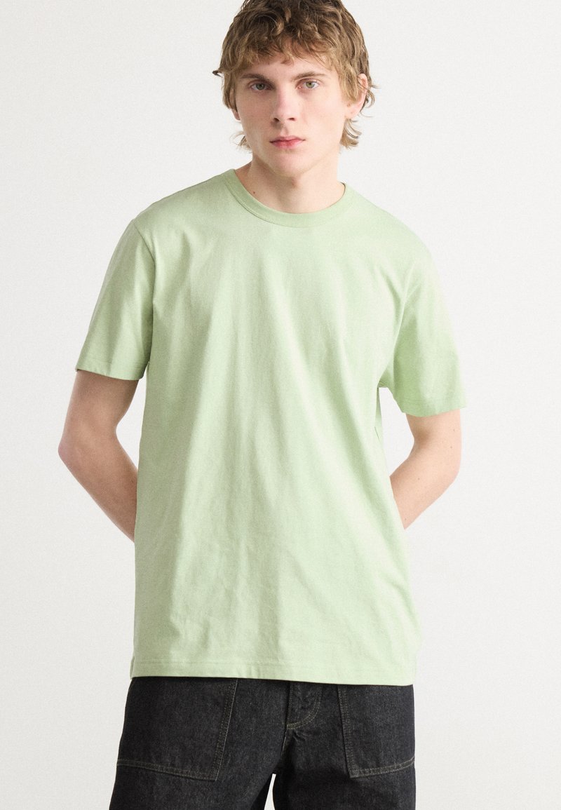 Light green cotton t-shirt with a crew neckline and short sleeves, paired with dark jeans. Minimalist design with no visible patterns or logos.