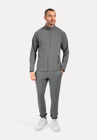 Grå atletisk træningsdragt med en lynlåslukket jakke og tapered bukser, der har en glat tekstur og elastiske manchetter. Båret med hvide sneakers.