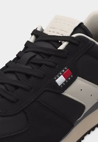 Baskets Tommy Jeans en noir et blanc avec des lacets noirs texturés et un logo rouge, blanc et bleu sur le panneau latéral.