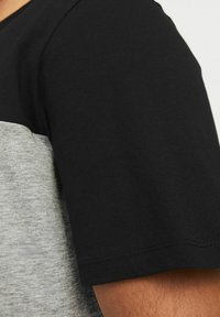 T-shirta kratkih rukava s crnim gornjim i sivo donjim dijelom, izrađena od mekog pamuka, s glatkom teksturom i jednostavnim detaljima šivanja.
