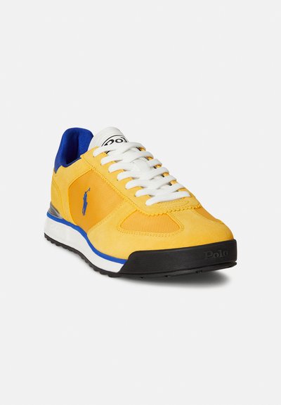 Żółty sneaker wykonany z zamszu i siateczki z niebieskimi akcentami. Posiada białe sznurowadła, czarną podeszwę oraz logo po bokach i na języku.