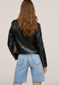 Veste en cuir noire au design court, avec des fermetures éclair sur les manches et une texture lisse, associée à un short en jean bleu clair.