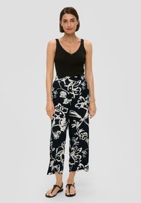 Un haut débardeur noir à côtes associé à un pantalon ample à motifs floraux bleu marine et blanc, avec une coupe décontractée et une longueur mi-mollet. Sandales noires.