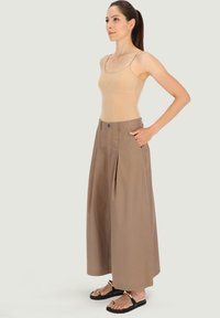Beżowy top na ramiączkach z cienkimi paskami, w połączeniu z szerokimi, jasnobrązowymi spodniami z przodu z fałdami. Uzupełniony czarnymi sandałami.