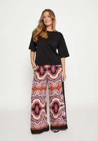 Zwart oversized T-shirt met korte mouwen, gecombineerd met kleurrijke, wijd uitlopende broek met patronen in roze, rood, blauw en zwarte accenten.