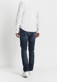Vit långärmad skjorta med knappmanschetter, i kombination med mörkblå denimjeans. Jeansen har en standard passform och femfickorsdesign, bärs med vita sneakers.