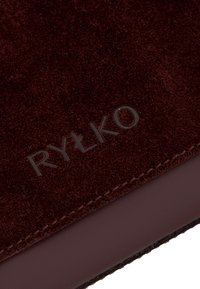 Burgundowa zamszowa tkanina o gładkiej fakturze, z wytłoczonym logo "RYŁKO" i eleganckimi krawędziami, podkreślająca teksturę i kunszt wykonania.