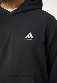 Hanorac negru din bumbac cu buzunar tip kangaroo, având un logo metalic cu trei dungi și textul "BASKETBALL" pe piept.