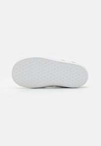 Shoe sole with a textured white rubber surface, featuring a geometric pattern for grip and durability. Flat, rounded shape with no additional details.