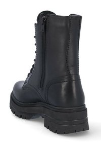 Botín negro de cuero con suela de goma gruesa, parte delantera con cordones y cremallera lateral. Presenta una textura suave y costuras reforzadas.