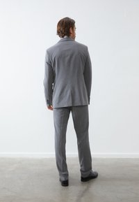 Grau Anzug mit maßgeschneidertem Design; verfügt über einen Schlitzt und passende Hosen sowie schwarze Schuhe. Glatte Textur, minimale Details.