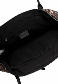 Mustan käsilaukun sisäosa, jossa on leopardikuosisetti, varustettuna vetoketjullisella taskulla ja avoimella lokeroilla. Pehmeä kangas, jossa näkyvät ompeleet.