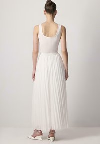 White sleeveless bodysuit paired with a long, pleated white skirt. The skirt features a flowy texture and a fitted waistband.
