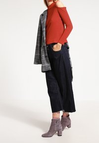 Geribbelde rode off-shoulder top, gecombineerd met donkere, wijde jeans met rafelige hems en grijze suède enkellaarsjes met ritsdetail.