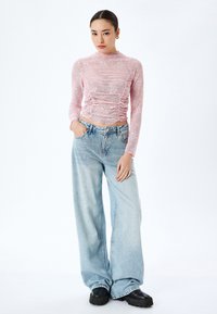 Rosa durchsichtige Langarmbluse mit gerafftem Design und Blumenmuster, kombiniert mit hellblauen weit geschnittenen Jeans und schwarzen Plateauschuhen.