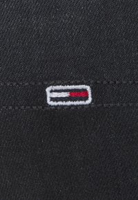 Czarna tkaninowa łatka z haftowanym logo flagi w kolorach czerwonym, białym i niebieskim. Szycie jest schludne i wyraźne.