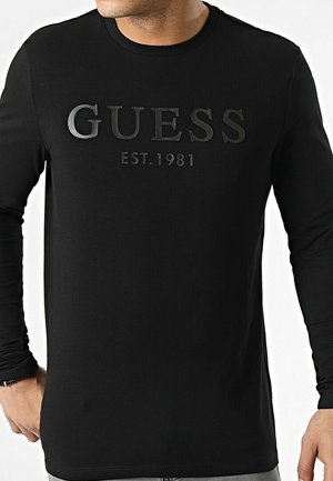 Schwarzes Langarmshirt mit erhabenem "GUESS"-Logo und "EST. 1981" in kontrastierender Farbe. Hergestellt aus glattem Stoff mit figurbetontem Schnitt.