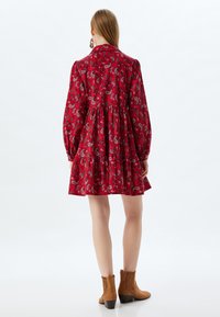 Rotes Paisleymuster-Kleid mit Kragen, langen Ärmeln und schichtigem Rock. Tragen mit braunen Stiefeletten, die einen strukturierten Stoff zeigen.