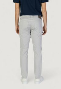 Pantalones gris claro de corte slim, con bolsillos traseros y una textura sutil. Combinados con zapatillas blancas para un look casual.