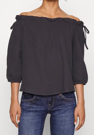 Blouse gris foncé, décolletée sur les épaules, avec un col froncé, des manches à nouer et des manches ballons de longueur moyenne en tissu léger et texturé.
