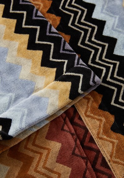 Tappeti texture con motivi a zigzag in tonalità di blu, nero, arancione e rosso. I materiali sembrano morbidi con una finitura pelosa.