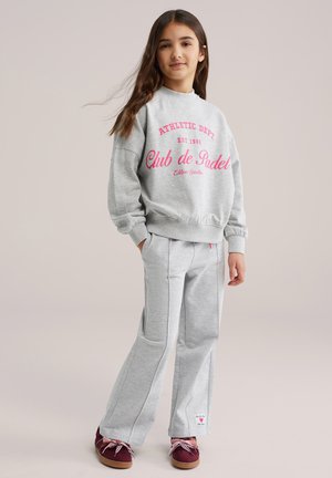 Sweatshirt gris avec texte rose, assorti à un pantalon de jogging gris. Détails comprenant des poignets élastiques et des poches latérales. Chaussures bordeaux avec lacets roses.