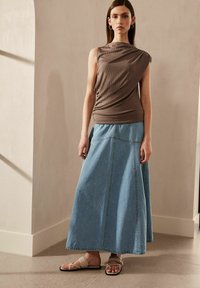 Brun ribbet ærmeløs top, blå denim maxi nederdel og beige flade sandaler. Glatte teksturer og kontrasterende farver skaber et lagdelt look.