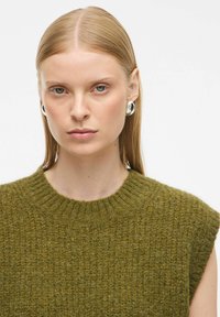 Olivno zeleni pleteni pulover z rebrastim okroglim izrezom in kratkimi rokavi, s strukturiranim vzorcem. Srebrni krožni uhani dopolnjujejo videz.