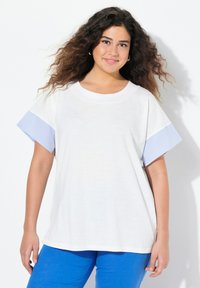 Valkoinen t-paita sinisillä raidallisilla lyhyillä hihoilla, pyöreä pääntie ja löysä istuvuus. Paidassa on sileä pinta ja rento muotoilu.