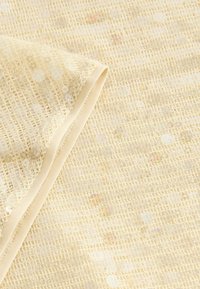 Béžový textil s mriežkovým vzorom, ktorý má jemný, textúrovaný povrch a nenápadné flitrové akcenty pozdĺž jedného okraja.