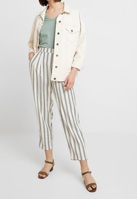 Beige denimjacka över en grön v-ringad t-shirt, tillsammans med randiga vida byxor. Bruna sandaler med remmar fulländar looken.