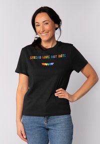 Zwart katoenen T-shirt met de tekst "SPREAD LOVE NOT HATE" in regenboogkleuren, met daaronder een meerkleurig hartontwerp.
