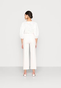 Blusa branca bordada com mangas bufantes, combinada com calças largas em tom creme. O conjunto apresenta uma textura leve e um design justo.