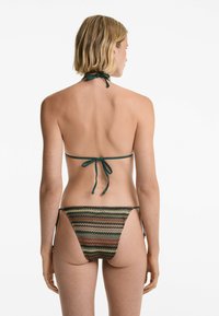 Bikini met een donkergroene striknek en een multicolore gebloemd bikinionderdeel met zigzagontwerpen. Het materiaal lijkt glad met minimale bedekking.