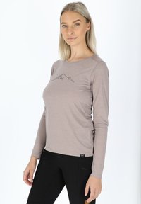 Camicetta a maniche lunghe marrone chiaro con una grafica di montagna grigia, caratterizzata da un collo rotondo e una texture liscia, abbinata a pantaloni neri.