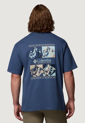 Uomo che indossa una maglietta blu Columbia Sportswear con quattro illustrazioni stilizzate di montagne sul retro.