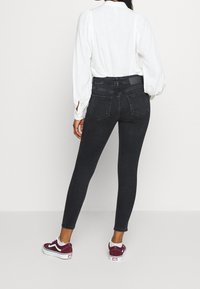Svarta skinny jeans med hög midja, bakfickor och en texturerad yta, kombinerat med en vit blus och vinröda sneakers.
