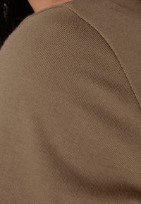 Tissu en laine brun tricoté montrant une texture côtelée et une couture d'épaule légèrement courbée, avec des détails de couture lisses visibles.