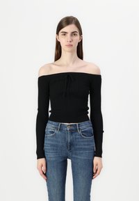 Sweater preto sem ombros com textura canelada e mangas longas, combinado com jeans de denim azul de cintura alta.