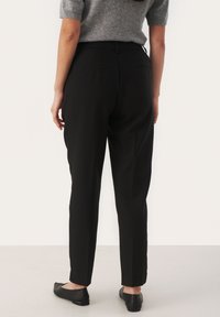 Black tailored trousers with a straight leg, featuring two small back pockets and a smooth finish. Worn with flat black shoes.