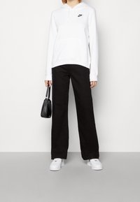 White Nike hoodie with a front pocket, paired with black wide-leg pants. Accessories include a small black handbag and white sneakers.